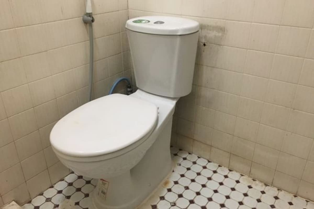 Des toilettes avec une cuvette et un réservoir blancs, une tuyauterie visible et un sol carrelé avec un motif hexagonal.