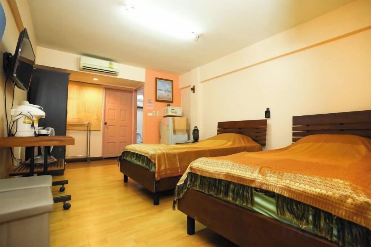 A hotel room with two beds, a desk with a chair, a television, and a refrigerator.
