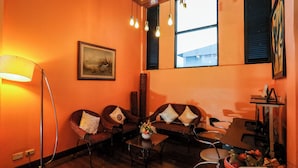 A cozy room with orange walls, a sofa set, a standing lamp, and a window with blinds. - Pjr Chateau (Bangkok)