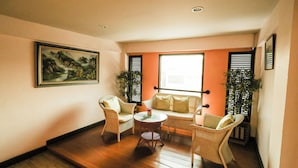 A cozy living room with wicker furniture, a painting on the wall, and a large window with blinds. - Pjr Chateau (Bangkok)