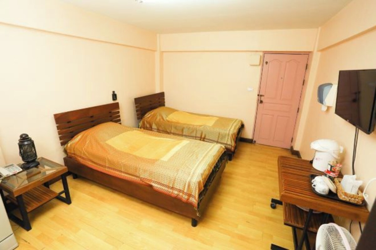 A hotel room with two single beds, a wooden desk, a small table, a TV, and a door.