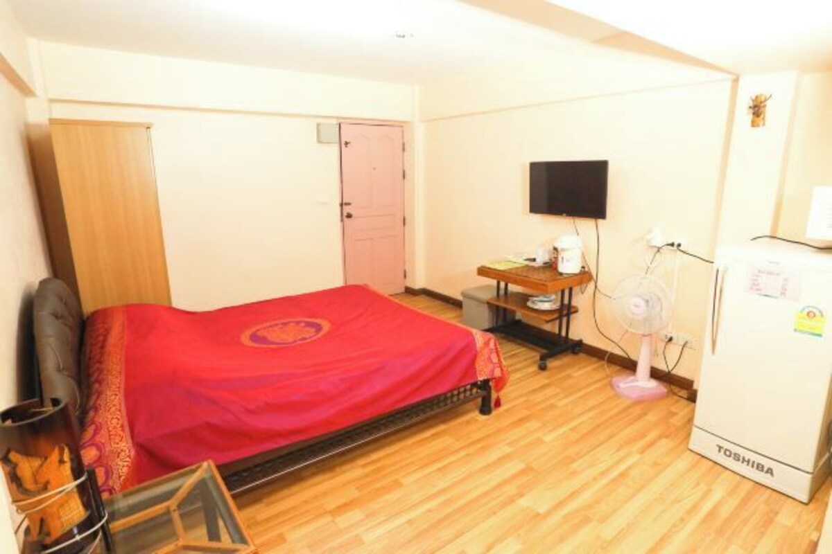 A room with a bed, a desk, a chair, a television, and a refrigerator.