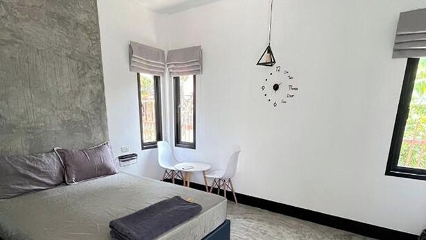 A modern bedroom with a large bed, a desk, and a hanging light fixture. - Baan Pak Sud Soi (Si Racha)