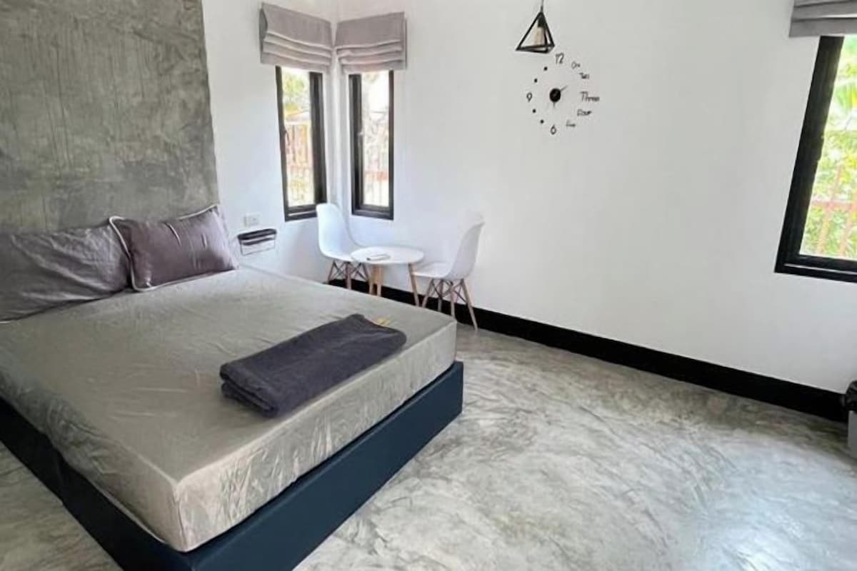 Une chambre à coucher moderne avec un grand lit, une petite table, deux chaises et une horloge au mur.
