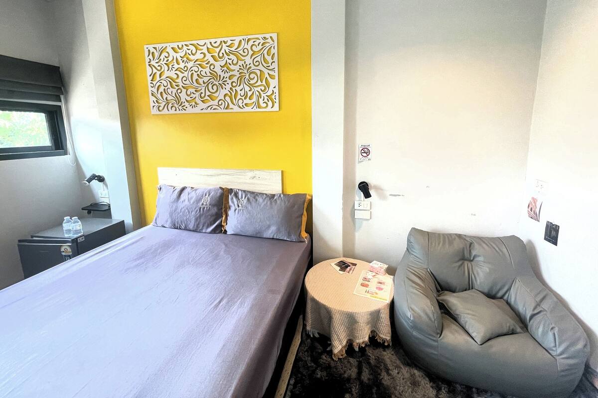 A bedroom with a bed, bedside table, and a small round table with a cushion.