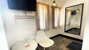 A small room with a TV mounted on the wall, a chair, a small table, and a mirror. - Baan Pak Sud Soi (Si Racha)