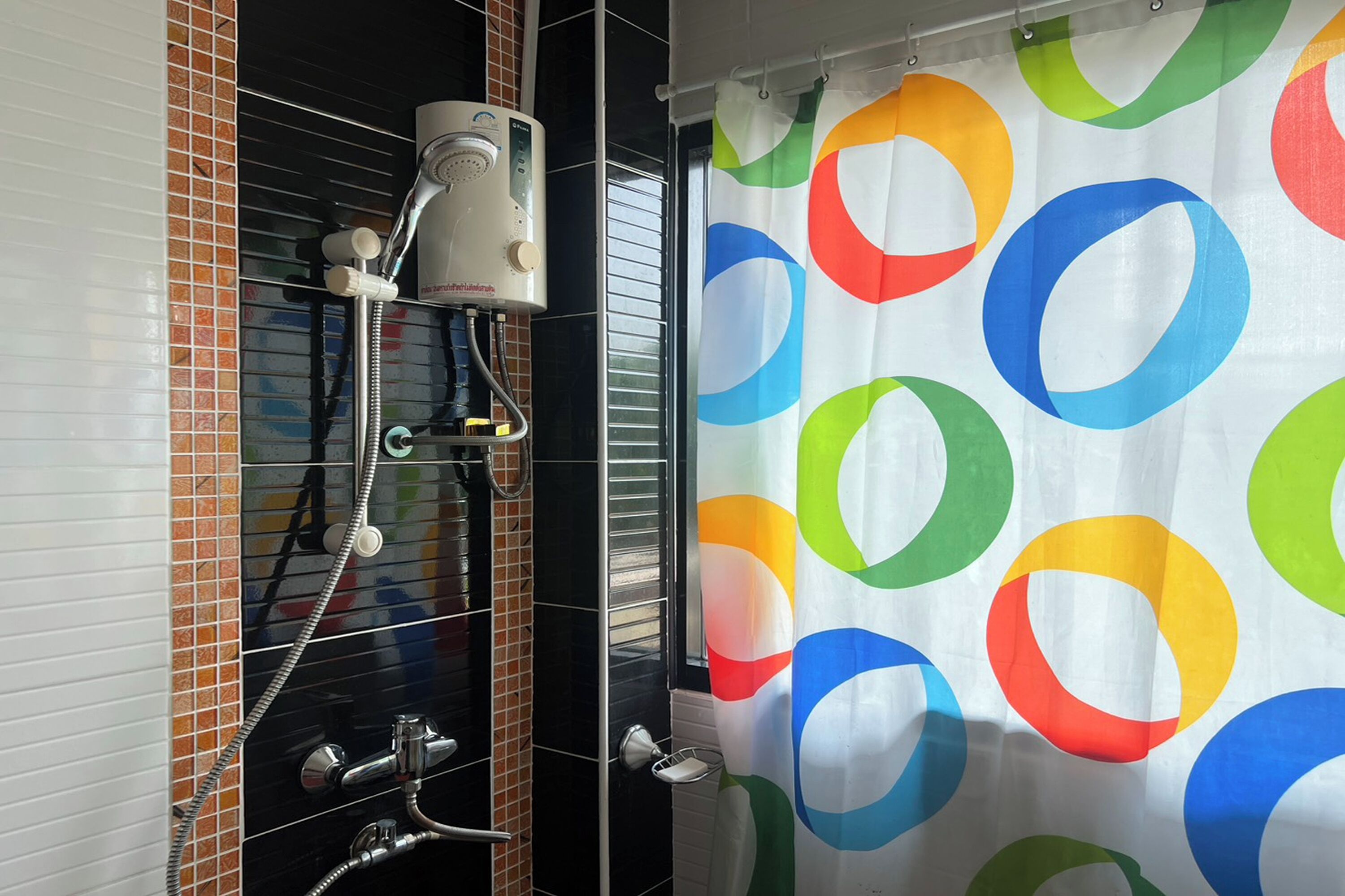 A bathroom with a shower, a towel rack, and a curtain with colorful circles.