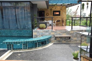 Uma área de piscina moderna ao ar livre, com parede de pedra, um banco de assento e um alpendre coberto com mesa e cadeiras.