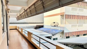 A balcony with a metal railing, a tiled floor, and a view of adjacent buildings with corrugated metal roofs. - Jamjuree Place (Khon Kaen)