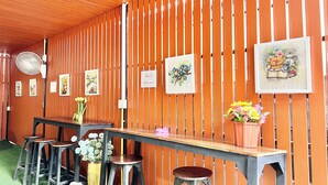 A wooden interior with a long table and stools, framed artwork on the walls, and a fan on the ceiling. - Jamjuree Place (Khon Kaen)