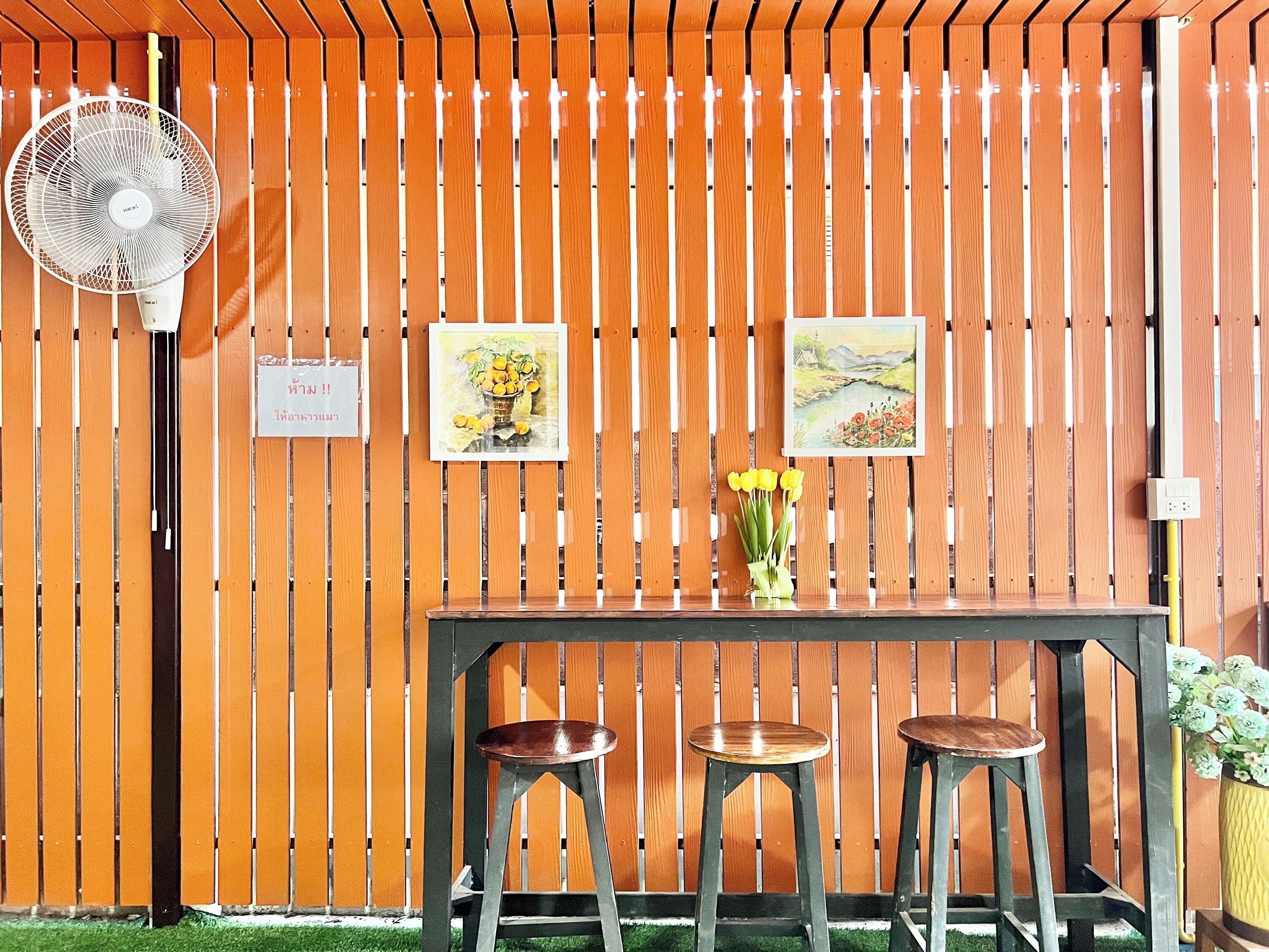 A wooden fence with a fan, two stools, and two framed paintings. - Jamjuree Place (Khon Kaen)