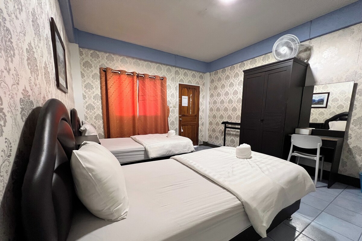 A hotel room with a bed, a desk, a chair, a wardrobe, and a fan.