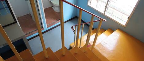 Una escalera con peldaños amarillos y barandilla roja que conduce a una habitación con inodoro y ventana.