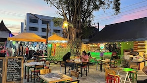 An outdoor café with wooden tables and chairs, a chalkboard menu, and a large tree in the background. - Bed Station Hostel Krabi (Krabi)