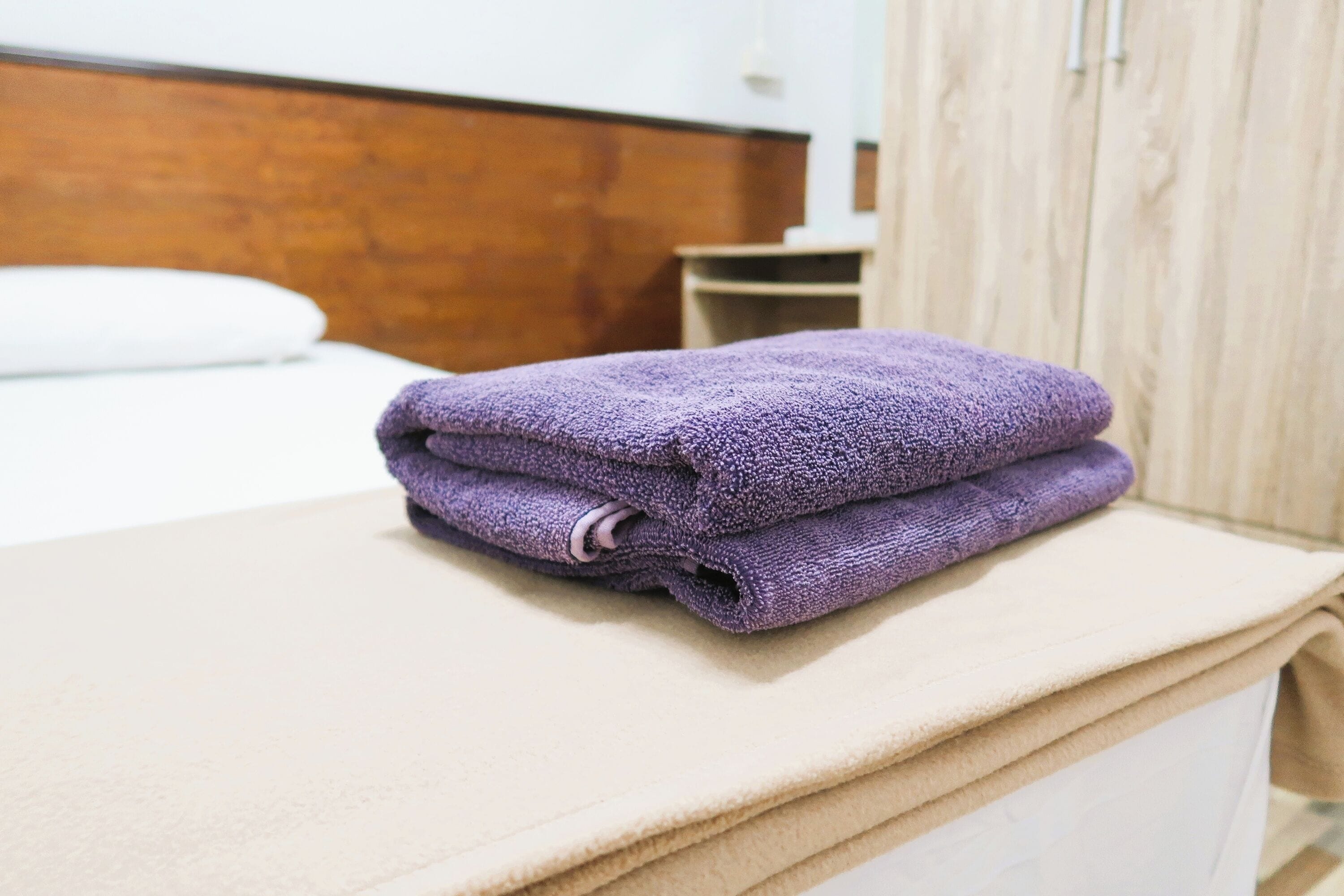 A neatly folded purple towel on a beige bedside table in a hotel room.