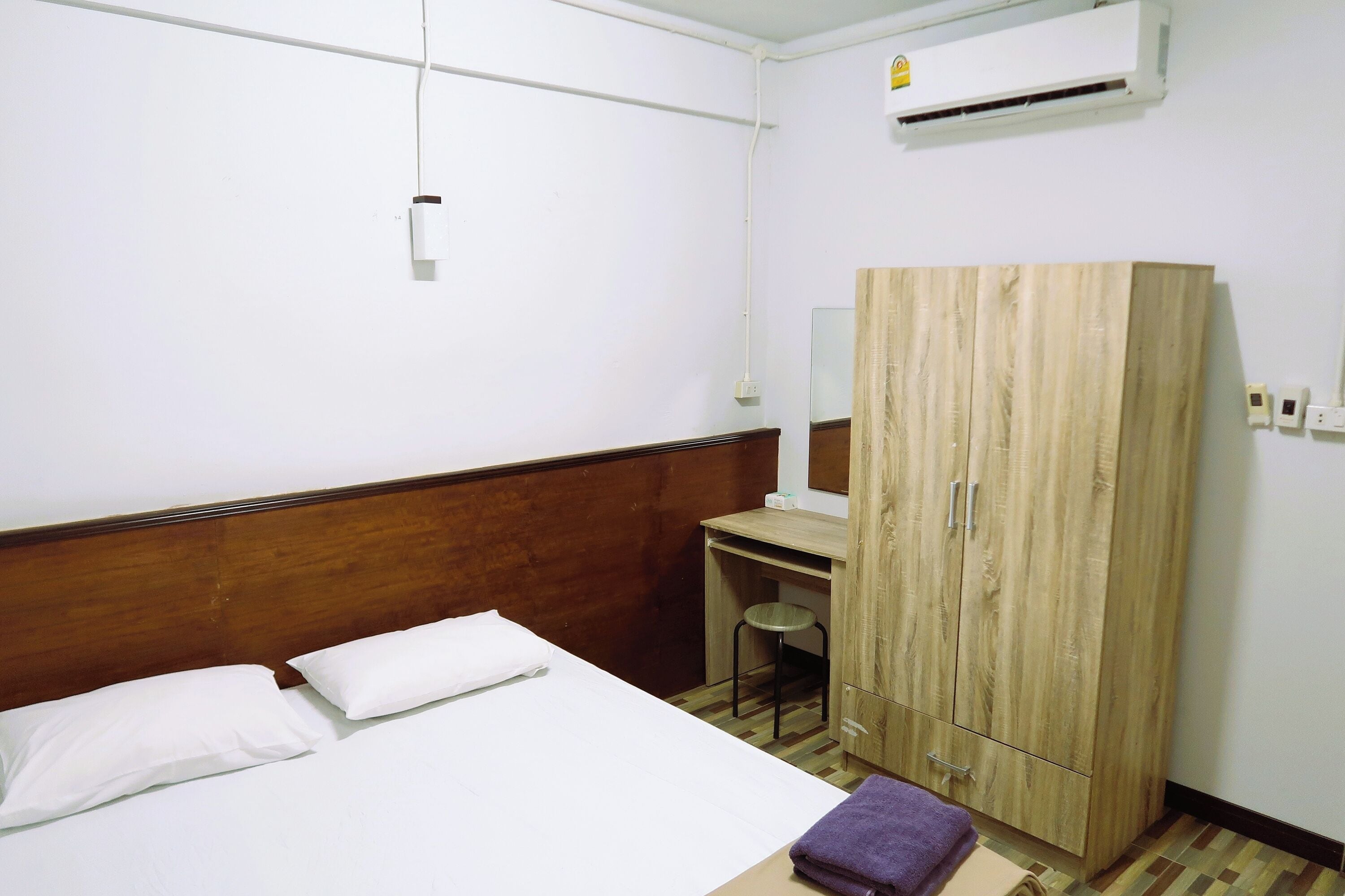 Una habitación de hotel con cama, escritorio, armario y un taburete.