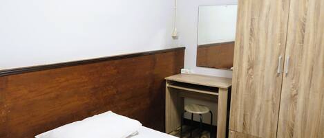 A hotel room with a wooden headboard, a bed with white linens, a small desk with a stool, and a wardrobe with a mirror.