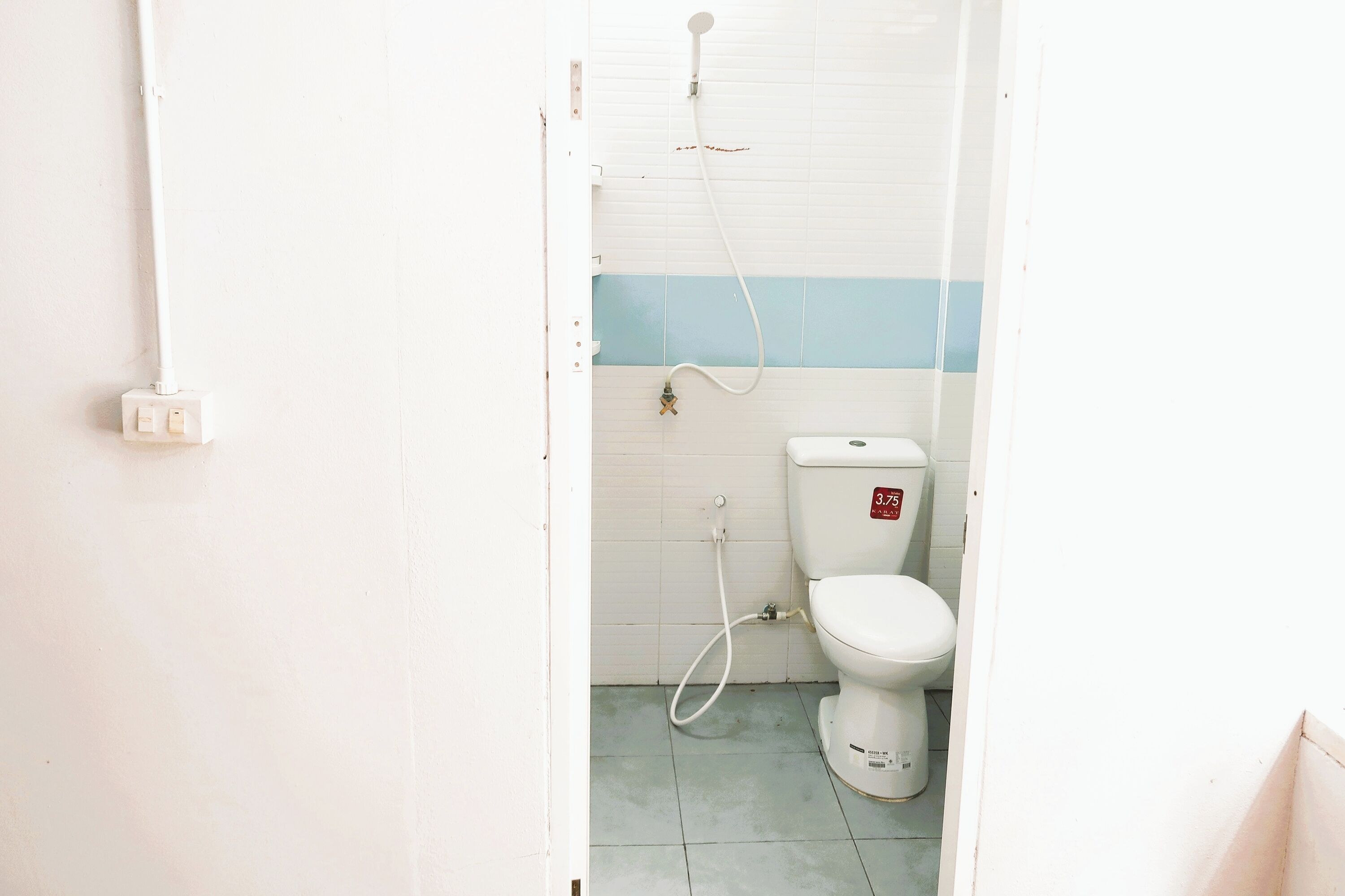 Un baño pequeño y sencillo con inodoro, ducha y una tubería de agua a la vista.