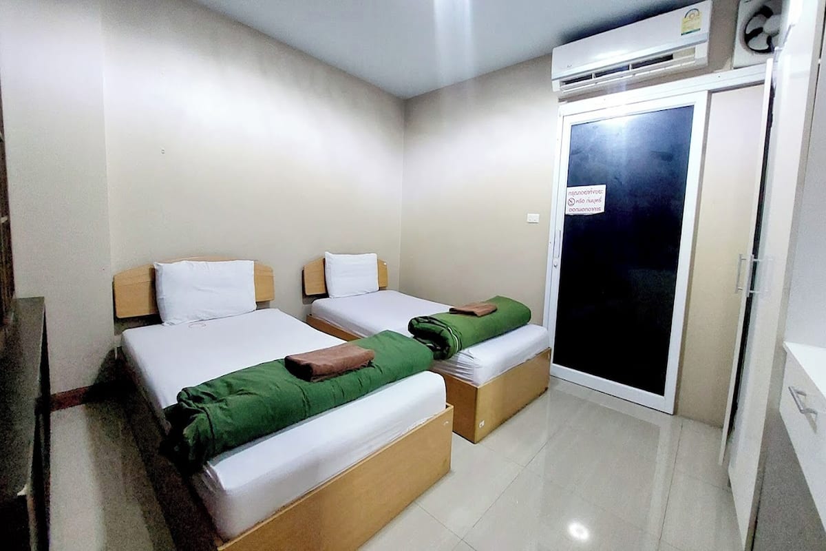 A hotel room with two beds, a wardrobe, and an air conditioning unit.