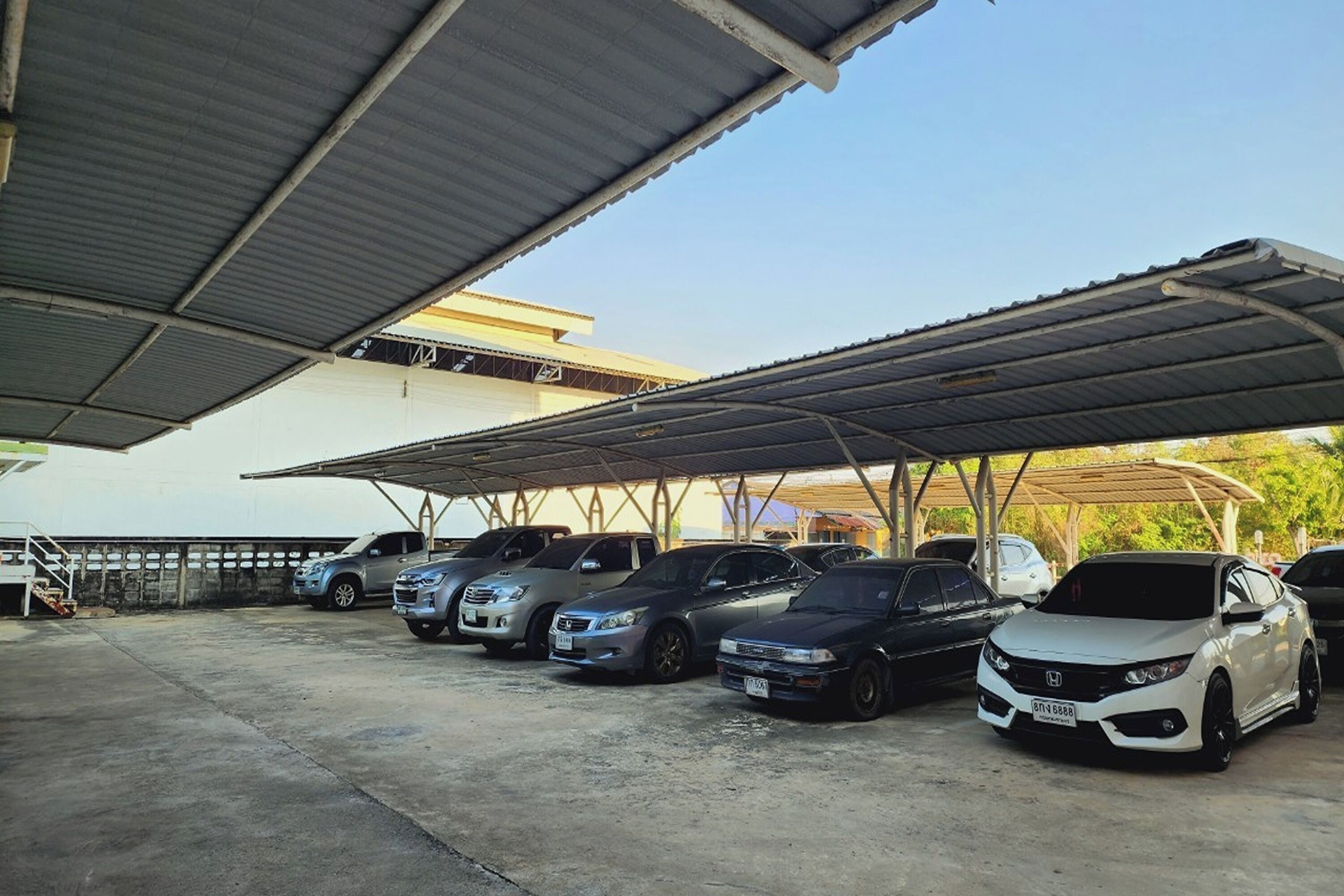 A covered parking area with several cars parked under a metal roof.