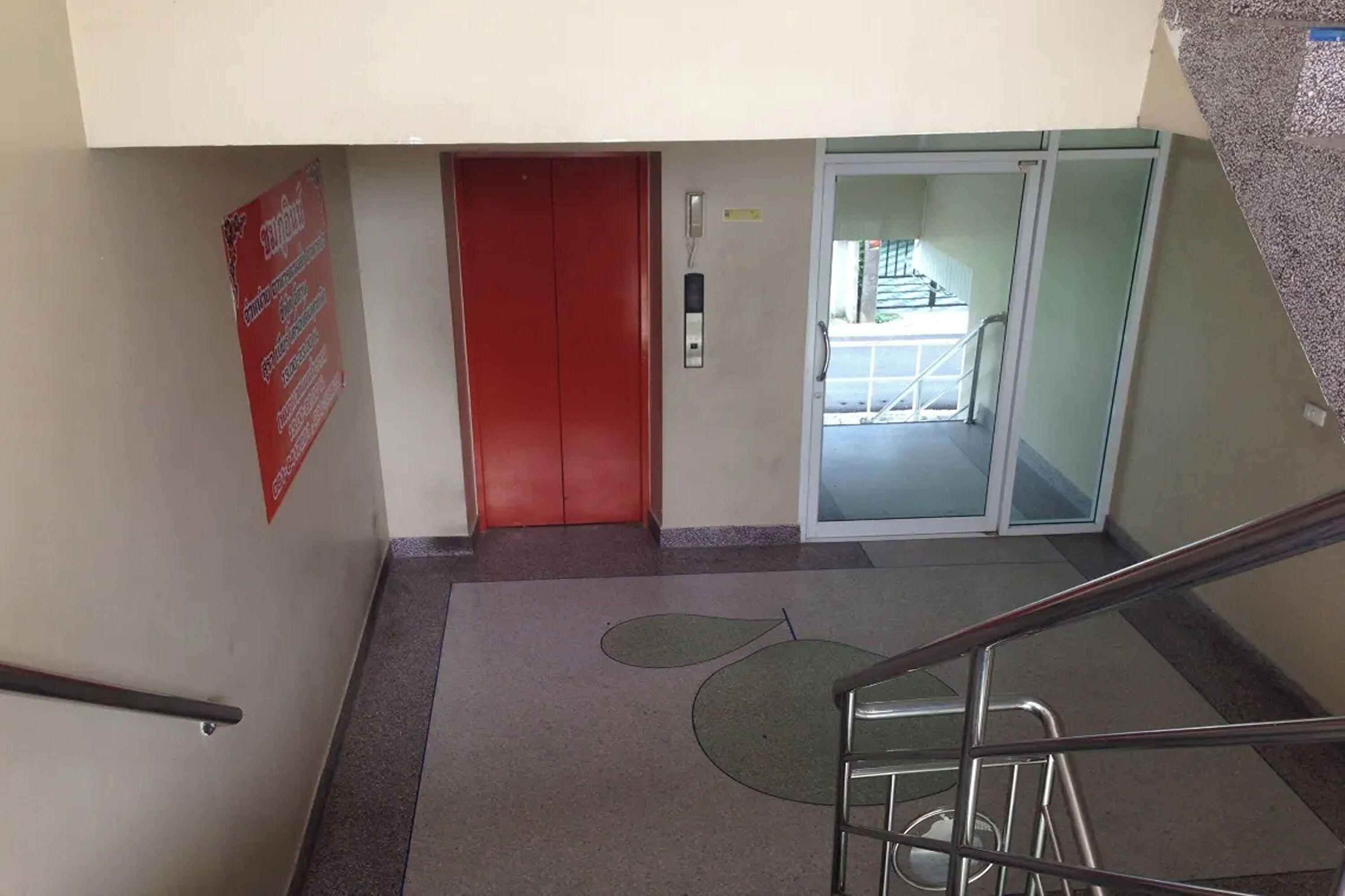 Una escalera con barandilla metálica que lleva a una puerta roja y una puerta de cristal.