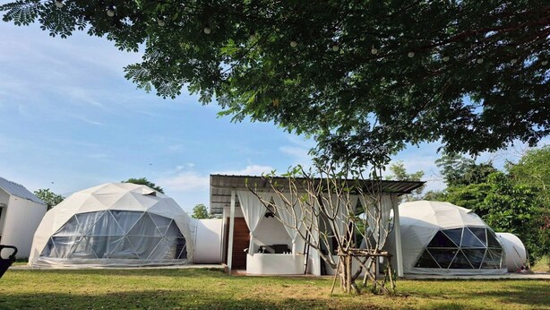 A series of geodesic dome structures, likely used for accommodation or events, with a grassy area in front and trees in the background. - Nanine Glamping By Zuzu (Cha-am)