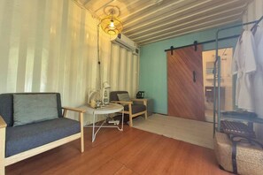 A cozy room with a sofa, a small table, a chair, and a wooden floor. - Nanine Glamping (Cha-am)