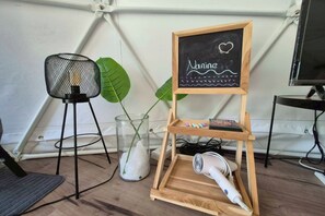A room with a wooden shelf holding a chalkboard with 'Narine' written on it, a hairdryer, and a small plant. - Nanine Glamping (Cha-am)