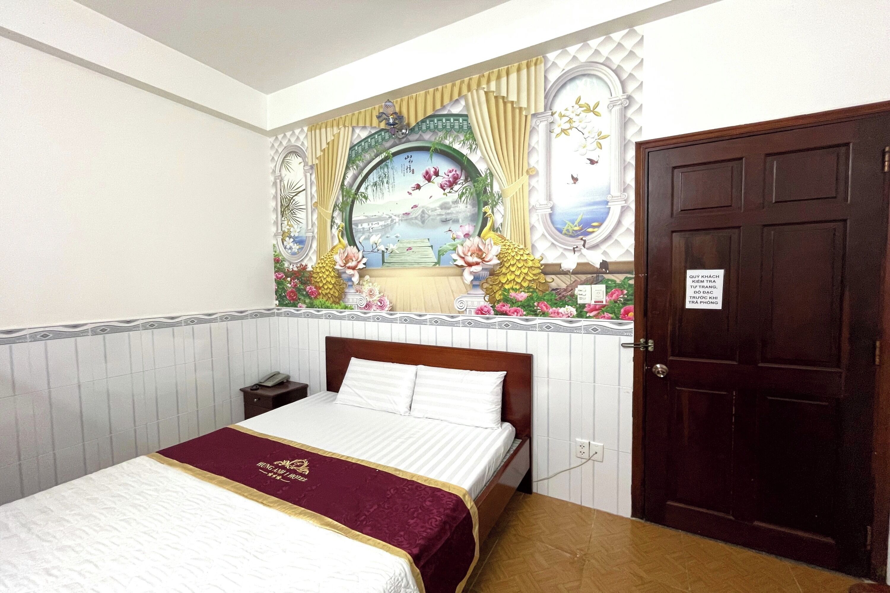 Habitación de hotel con cama, mesita de noche, puerta de madera y un mural decorativo.