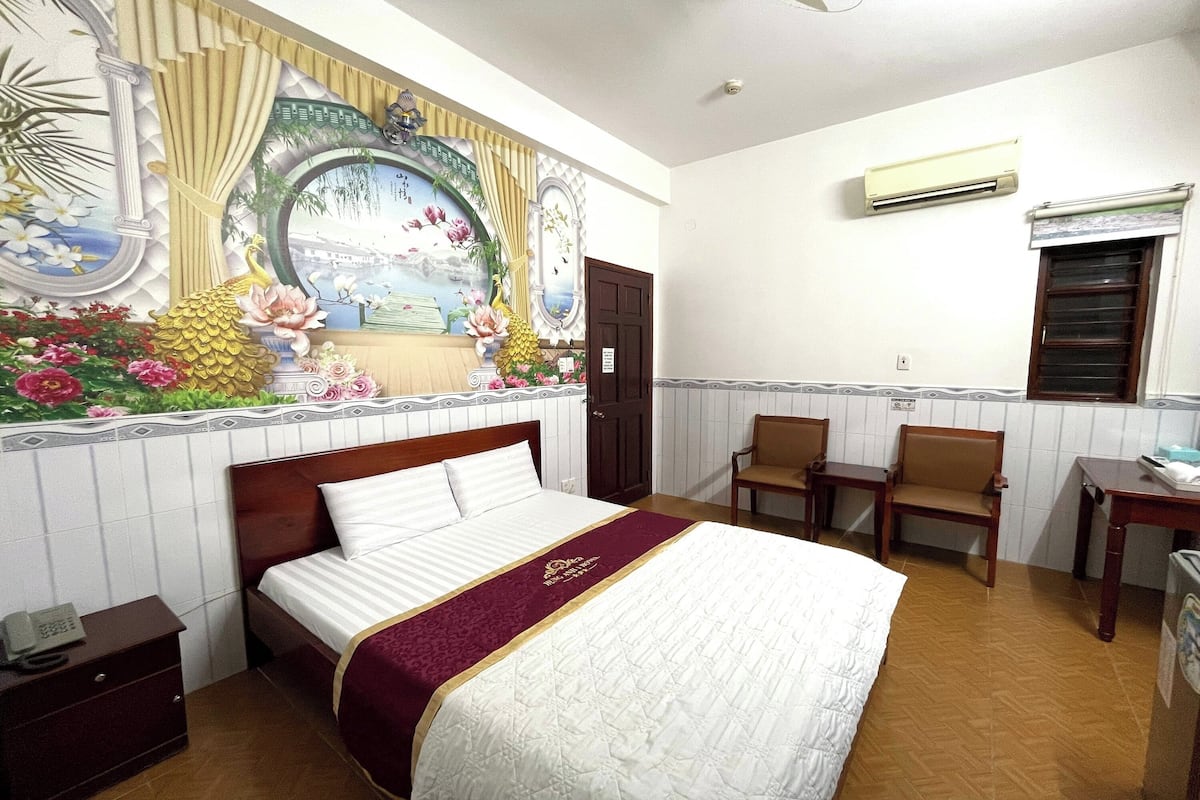A hotel room with a bed, a desk, a chair, and a wall mural.