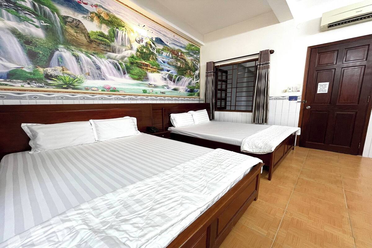 A hotel room with two beds, a mural of a waterfall, a wooden door, and a tiled floor.