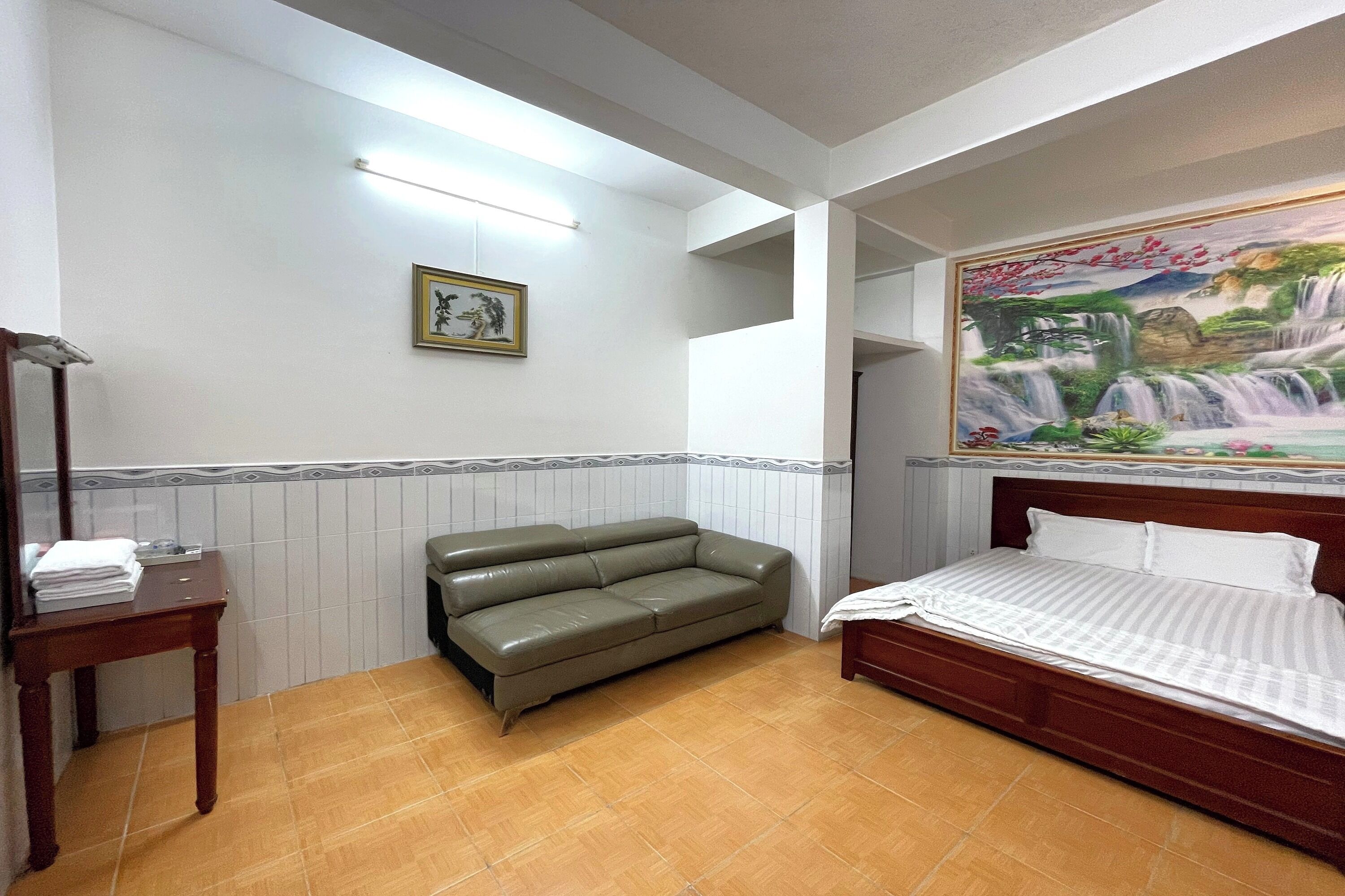 A bedroom with a bed, a green sofa, a wooden table, and a framed picture on the wall.