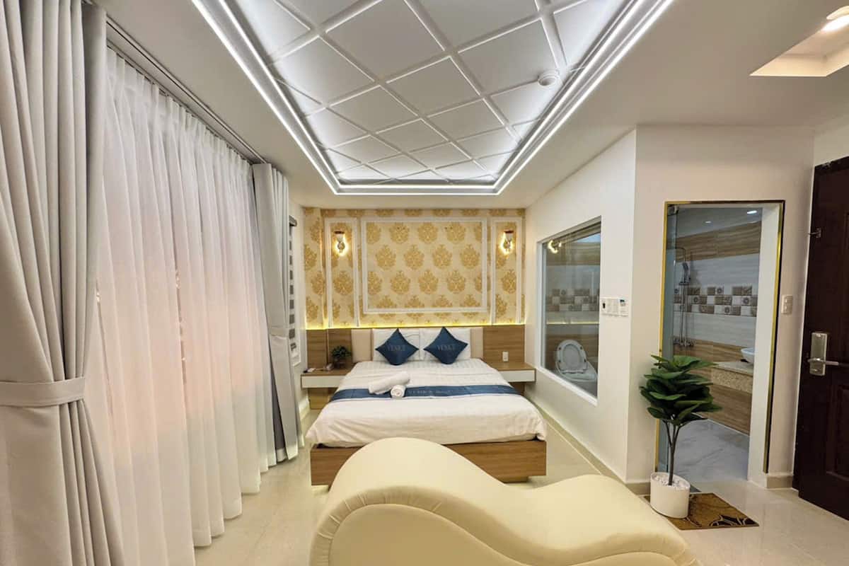 Un dormitorio moderno con una cama grande, un sofá blanco original y un techo con tragaluces.