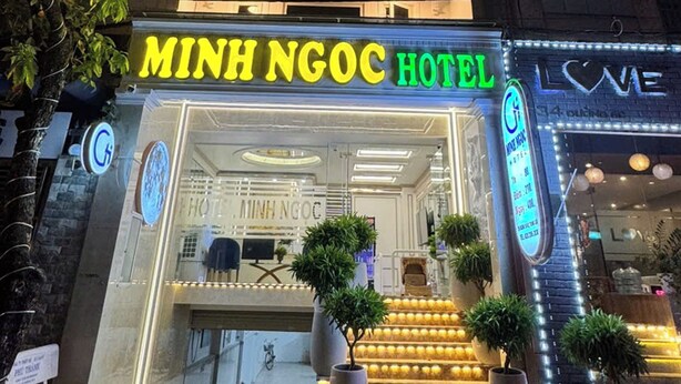 Hotel Minh Ngoc con un letrero de neón brillante, un mostrador de recepción y una escalera que lleva a la entrada.