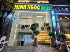 Hotel Minh Ngoc com um letreiro de neon vibrante, um balcão de recepção e uma escadaria que leva à entrada.