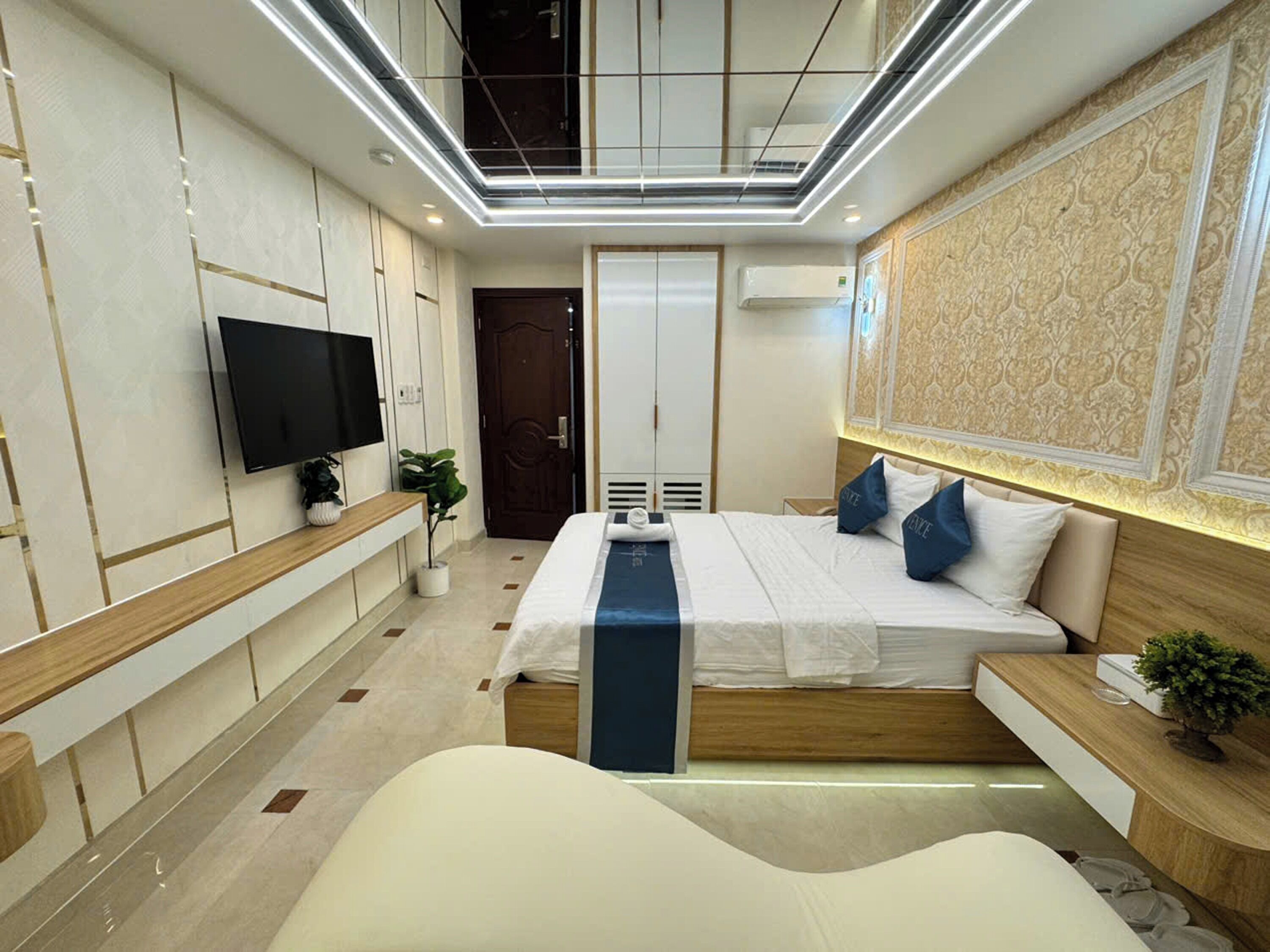 A modern hotel room with a large bed, a television, a desk, and a decorative wall.