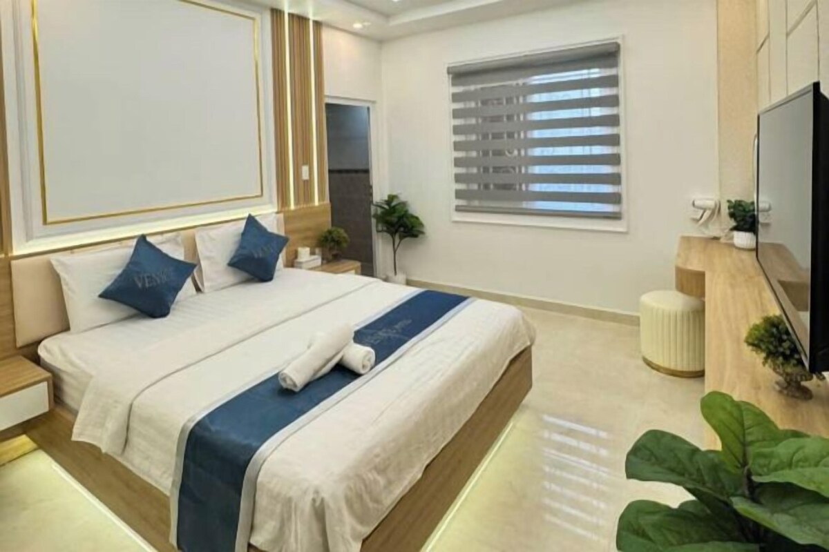 Un dormitorio moderno con una cama grande, mesitas de noche, un televisor y una ventana con persianas.