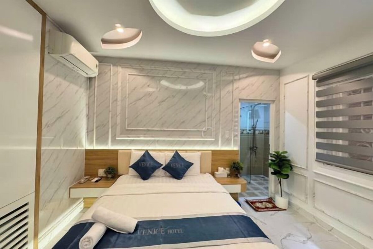 Una habitación de hotel con cama, mesitas de noche, un espejo y una zona de ducha.
