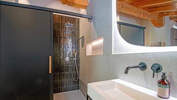 A modern bathroom with a large mirror, a white sink, and a shower area.