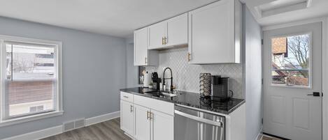 A modern kitchen with white cabinets, stainless steel appliances, and a black countertop.