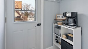 Un hall d’entrée propre et moderne, avec une porte blanche, un coin café équipé d’une machine à café et une petite étagère agrémentée d’objets décoratifs.