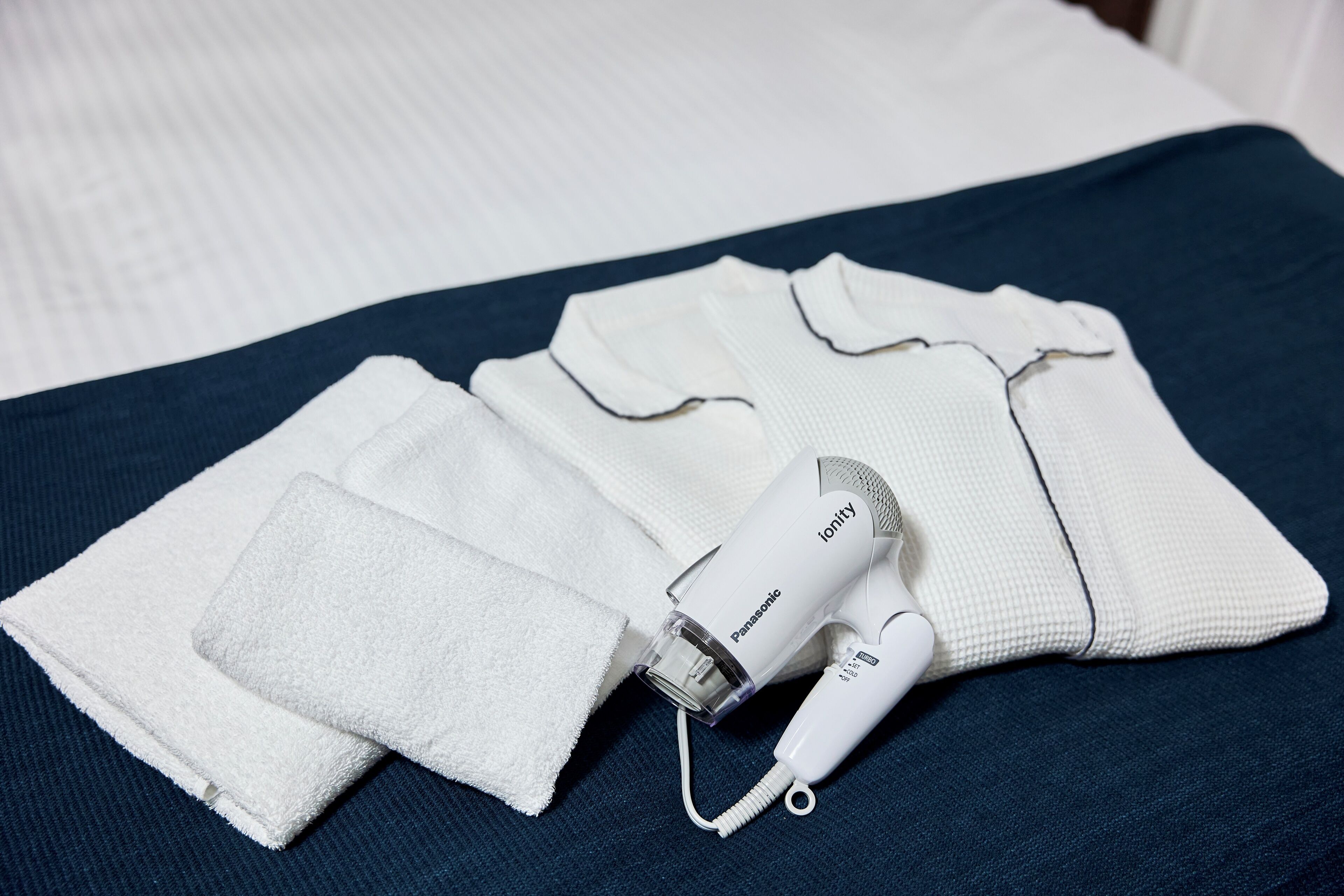 Ein Panasonic-Haartrockner und gefaltete Handtücher auf einem Bett.