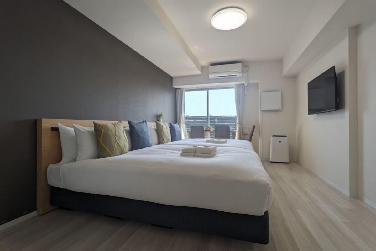 A modern hotel room with a large bed, a flat-screen TV, and a view of the city through the window.