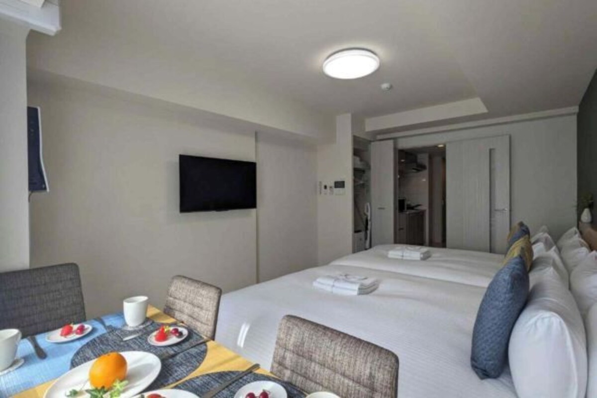 A hotel room with a bed, a TV mounted on the wall, a dining table with plates of food, and a chair.