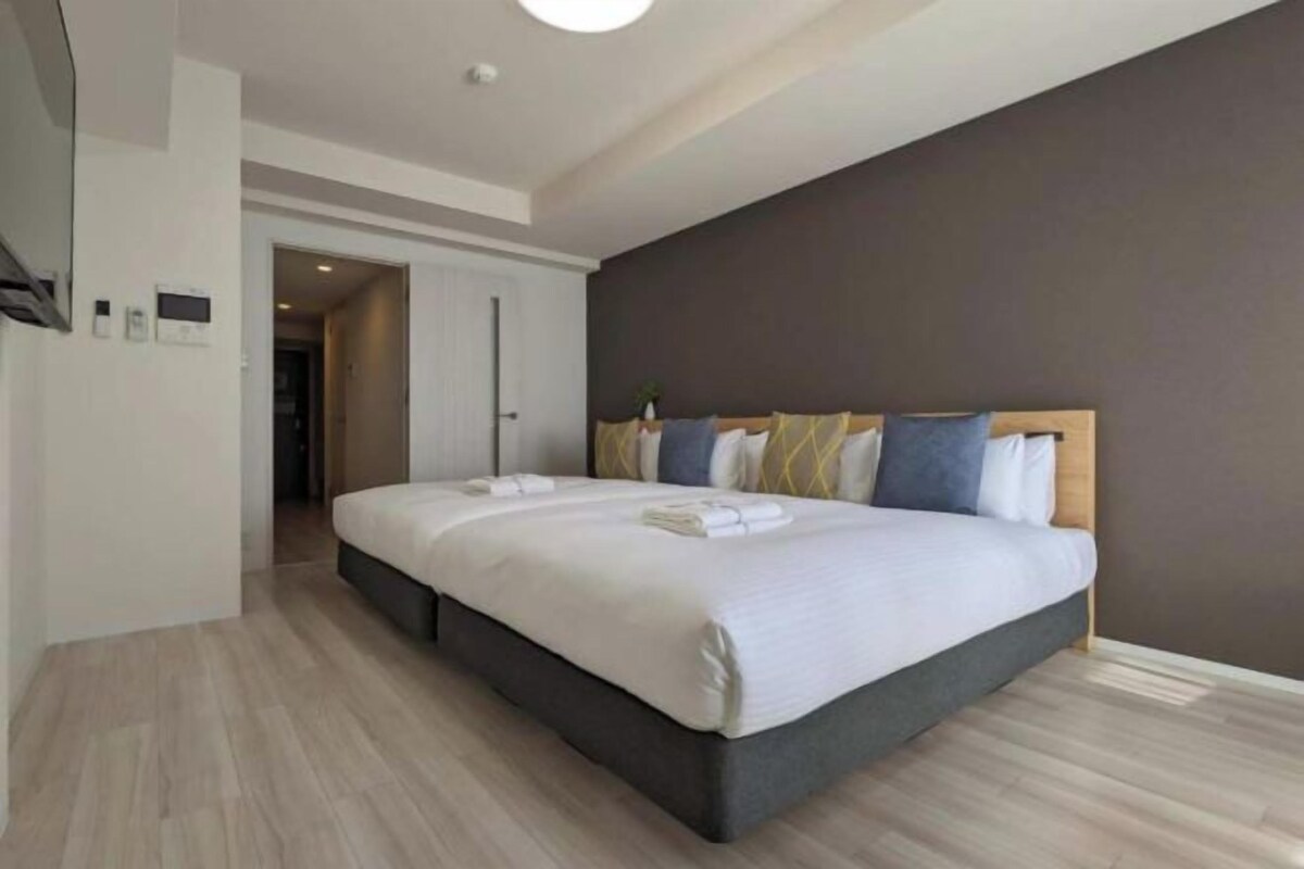 A modern hotel room with a large bed, a dark headboard, and a wooden floor.