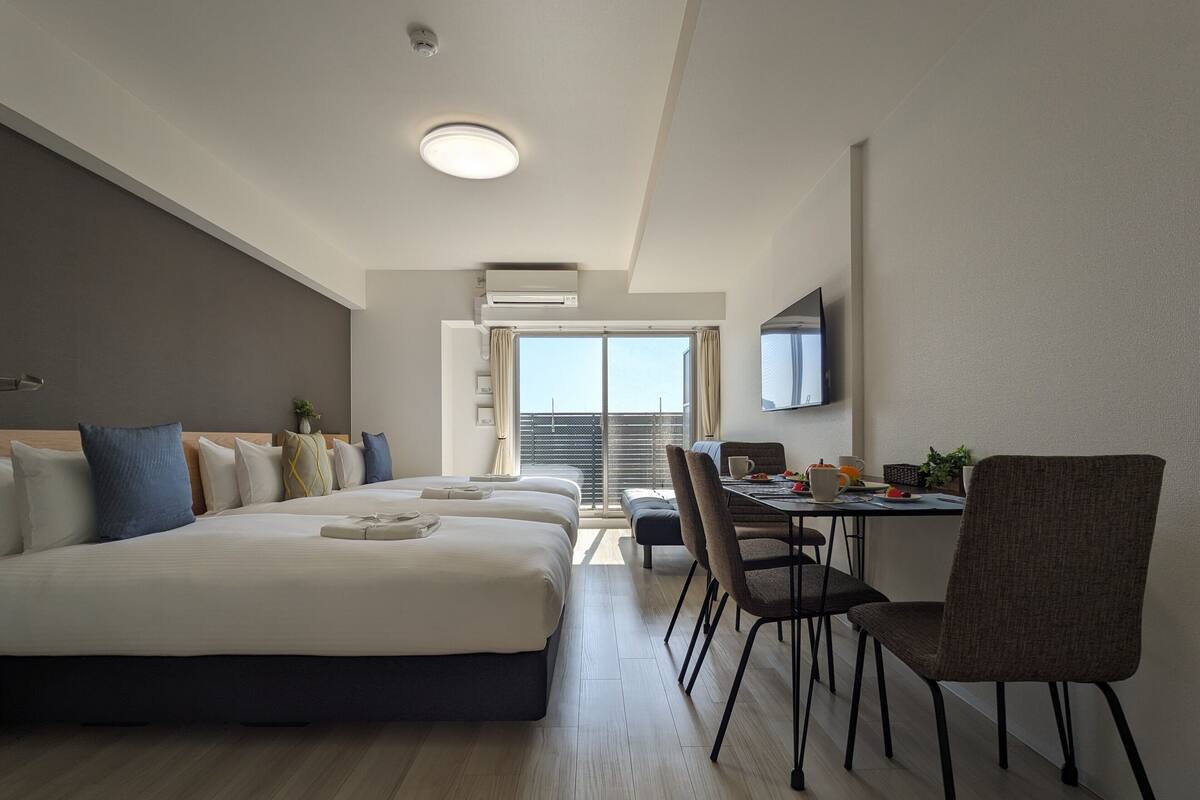Une chambre d’hôtel moderne dotée d’un grand lit, d’un coin repas avec une table et des chaises, d’un téléviseur à écran plat et d’un balcon avec vue.