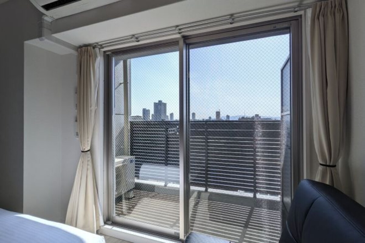 A hotel room with a large window, a bed, and a chair.