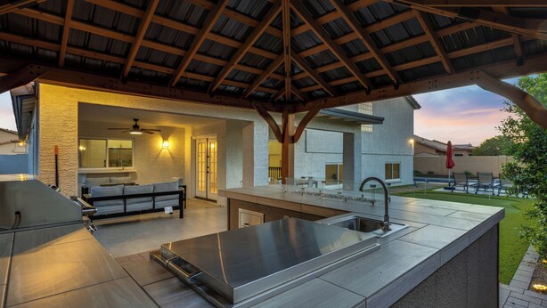 A modern outdoor kitchen with a large island, built-in seating, and a covered patio area. - NEW! Luxe Vacation Getaway - heated pool and putting green (Peoria)