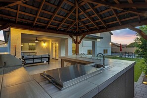 A modern outdoor kitchen with a large island, built-in seating, and a covered patio area. - NEW! Luxe Vacation Getaway - heated pool and putting green (Peoria)