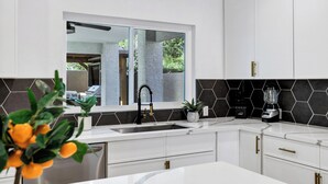 A modern kitchen with white cabinets, a black backsplash, and a window overlooking a garden. - NEW! Luxe Vacation Getaway - heated pool and putting green (Peoria)